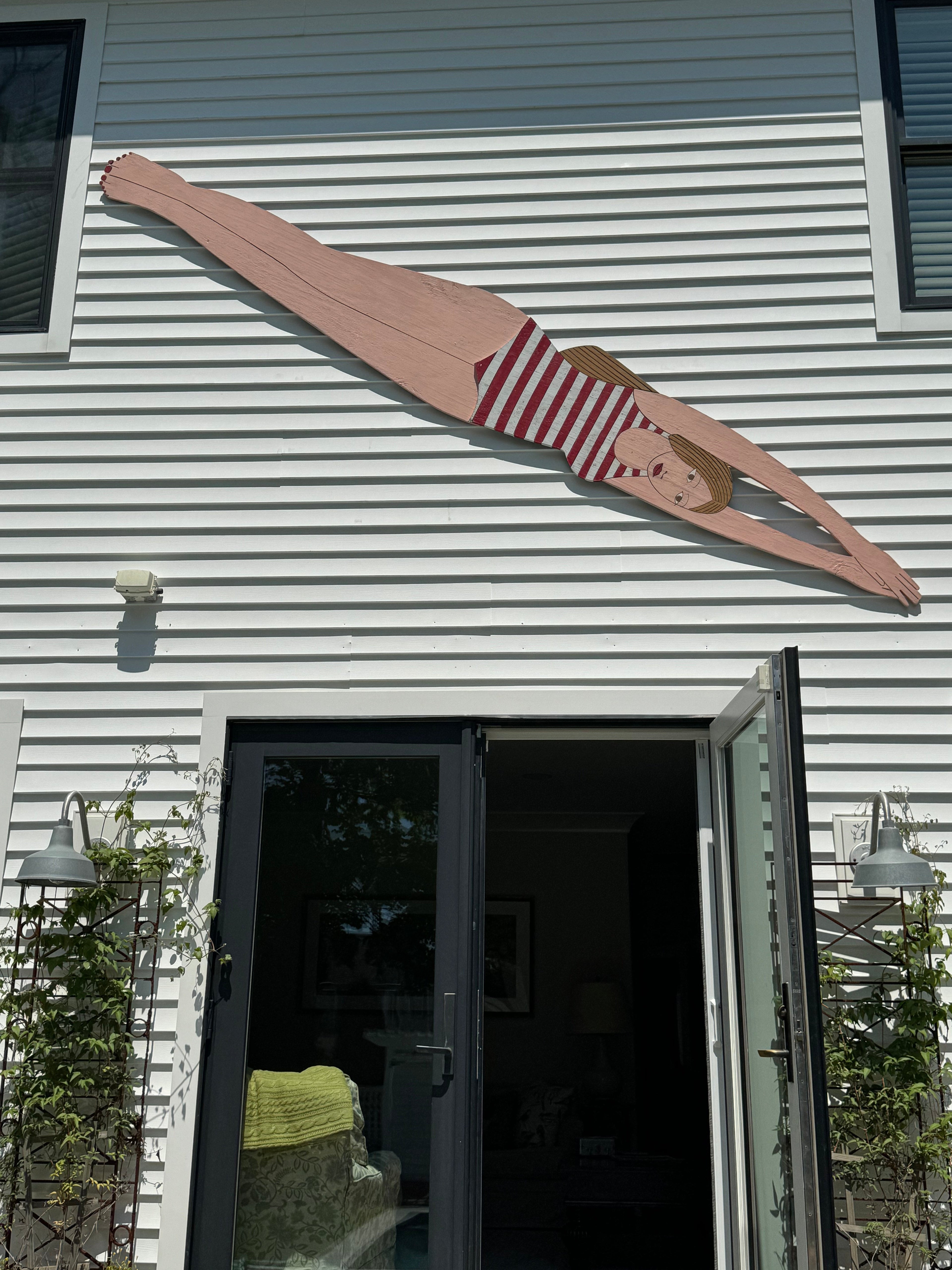 Wooden cutout of a women in a swimsuit attached to a building exterior by a pool
