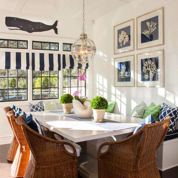 Folk Whale wooden wall art displayed in a bright coastal dining room with wicker chairs and navy accents interior design by HavenAmerica.